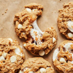 A close-up image of one of the white chocolate milkshake cookies, sitting on a piece of parchment paper and broken in half