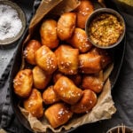 A basket of the air fryer pretzel bites, sitting on a countertop alongside a small bowl of grainy mustard