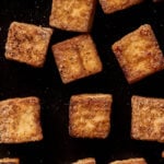 Golden-brown, crispy tofu cubes scattered on a dark surface.