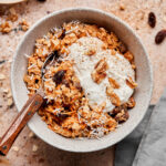 A bowl of the carrot cake cauliflower oats, on a countertop, with ingredients scattered beside it.
