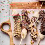 A cutting board lined with parchment paper and four of the frozen chocolate banana pops on them