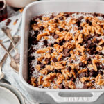 A baking dish full of the German chocolate cake overnight oats, sitting on top of a linen napkin. Plates, spoons, and a smaller bowl of oats can be seen in the background