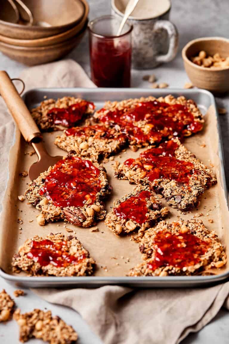 A baking sheet lined with parchment paper and topped with the PB&J granola clusters