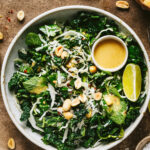 A large bowl of the copycat Hillstone emerald kale salad, with a lime wedge and a small bowl of dressing resting inside the salad bowl