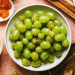 A bowl of the frozen Tajin grapes, sitting on a countertop. A cutting board with juiced lemons can be seen in the background.
