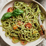 A large bowl of the vegan pistachio pesto zucchini noodles, topped with fresh basil and sitting on a countertop