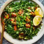 A large bowl of the kale tabouleh salad, with fresh lemon wedges and a wooden spoon sticking out of it