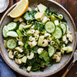 A bowl of the simple green pasta salad with lemon tahini dressing, sitting on a countertop with a lemon wedge.