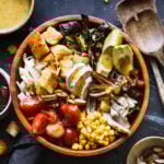 A LARGE BOWL OF THE COPYCAT HILLSTONE MACHO SALAD, ON A COUNTERTOP WITH A SMALL BOWL OF CORN, A BOWL OF SLIVERED ALMONDS, AND A BOWL OF DRESSING