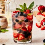 A tall glass of the gut healthy mixed berry mocktail, topped with fresh mint and sitting on a countertop