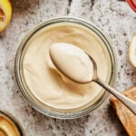 A jar of the homemade mayonnaise, sitting on a countertop. A spoon can be seen lifting some of the mayo out of the jar.
