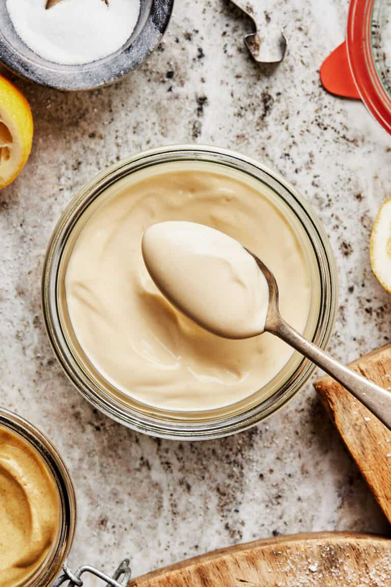 A jar of the homemade mayonnaise, sitting on a countertop. A spoon can be seen lifting some of the mayo out of the jar.