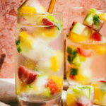 Two tall glasses of water, with the fruity ice cubes stacked high inside of them