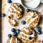 A few of the lemon blueberry protein breakfast bites, on a sheet of parchment, with a bowl of icing next to them