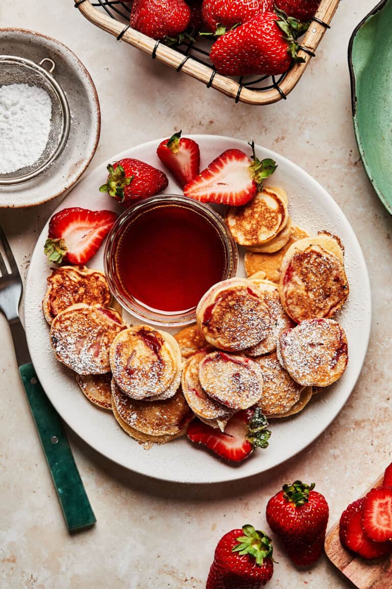 A plate of the strawberry pancake dippers, on a plate with a bowl of maple syrup and fresh strawberries