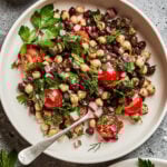 A large bowl, sitting on a countertop, with the balela salad inside of it. A fork rests inside the bowl.