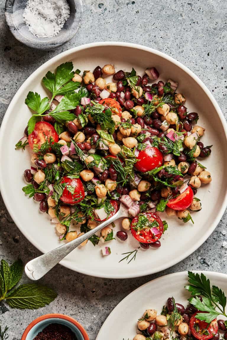 A large bowl, sitting on a countertop, with the balela salad inside of it. A fork rests inside the bowl.