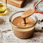 A large jar filled with the homemade tahini, with a spoon dunked into it