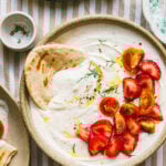 A bowl of the strawberry tomato whipped feta dip, sitting on a tabletop with a piece of flatbread dipped into it.