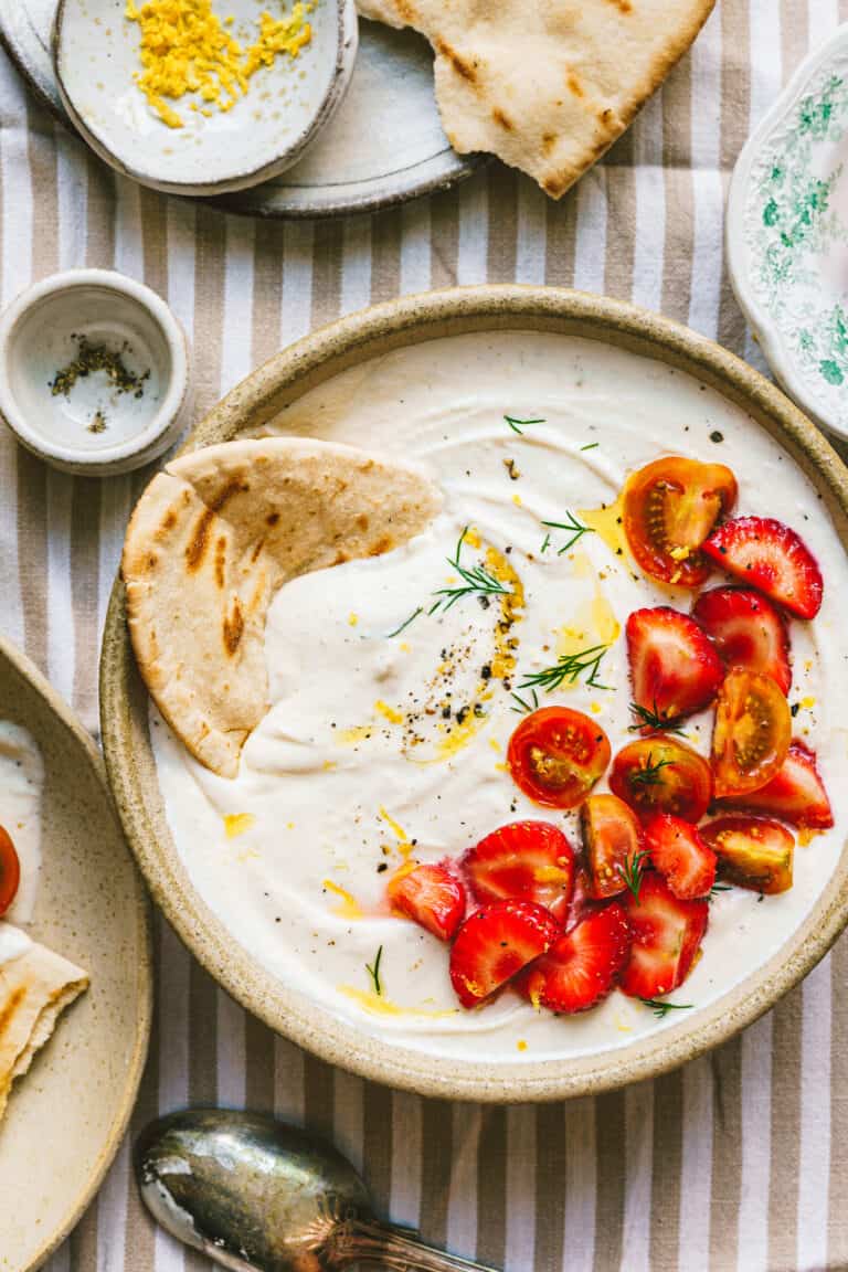 A bowl of the strawberry tomato whipped feta dip, sitting on a tabletop with a piece of flatbread dipped into it.