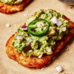 A close-up image of one of the spicy smashed avocado hash brown toasts, placed on a sheet of parchment paper