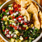 A bowl of the feta avocado dip, sitting on a cutting board, with a few chips sitting inside of the bowl.