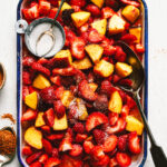 A tray of the sweet & sour tajin peaches & strawberries, sitting on a countertop. A bowl of sugar sits nestled into the peaches and strawberries