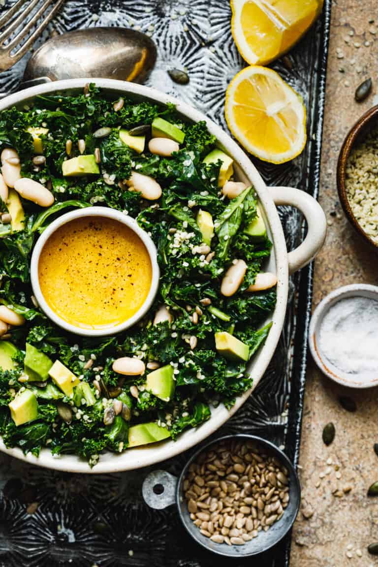A big bowl of the copycat Erewhon kale and white bean salad, sitting on a countertop, surrounded by ingredients