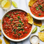 Two bowls of the quick & easy blender salsa, sitting on a countertop, surrounded by tortilla chips