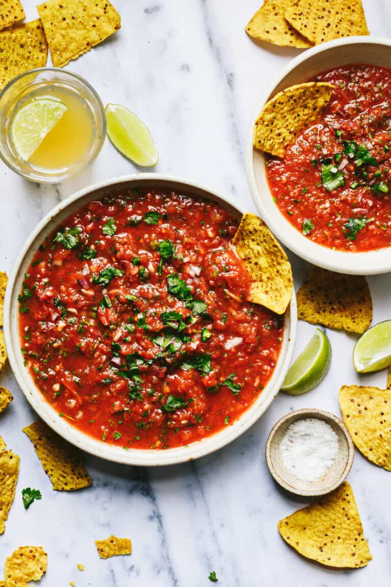 Two bowls of the quick & easy blender salsa, sitting on a countertop, surrounded by tortilla chips