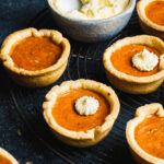 A tray of the best ever mini pumpkin pies, sitting alongside a bowl of whipped cream