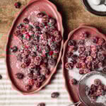 Two large plates of the sugar free frosted cranberries, sitting on a countertop with a small bowl of sugar
