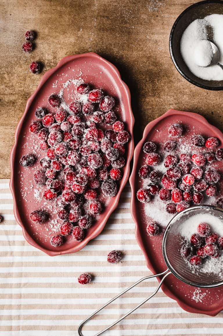 Two large plates of the sugar free frosted cranberries, sitting on a countertop with a small bowl of sugar