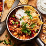 A big bowl of the loaded vegetarian quinoa chili, sitting on a cutting board surrounded by ingredients