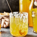 |A glass of the morning glow-up tonic, sitting on a countertop with a larger jar of the tonic sitting on the counter behind the glass