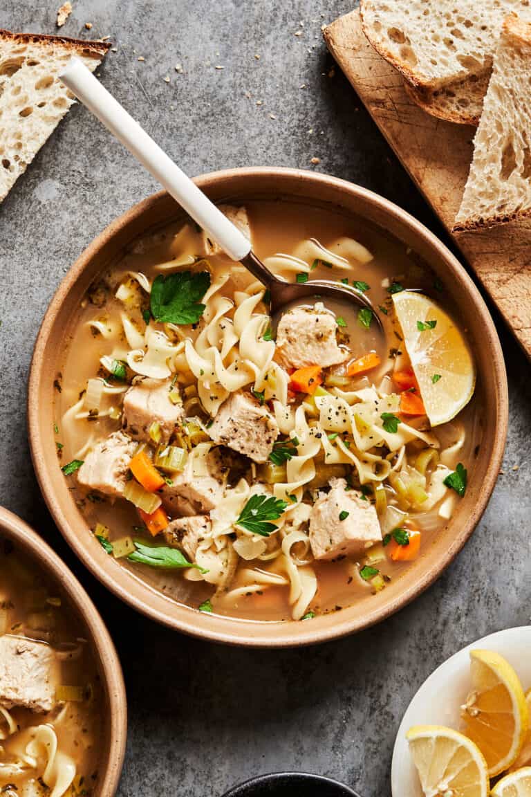 A bowl of the cozy turkey noodle soup, sitting on a countertop