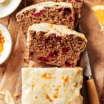 The best ever cranberry orange loaf, sitting on a countertop, sliced into a few slices