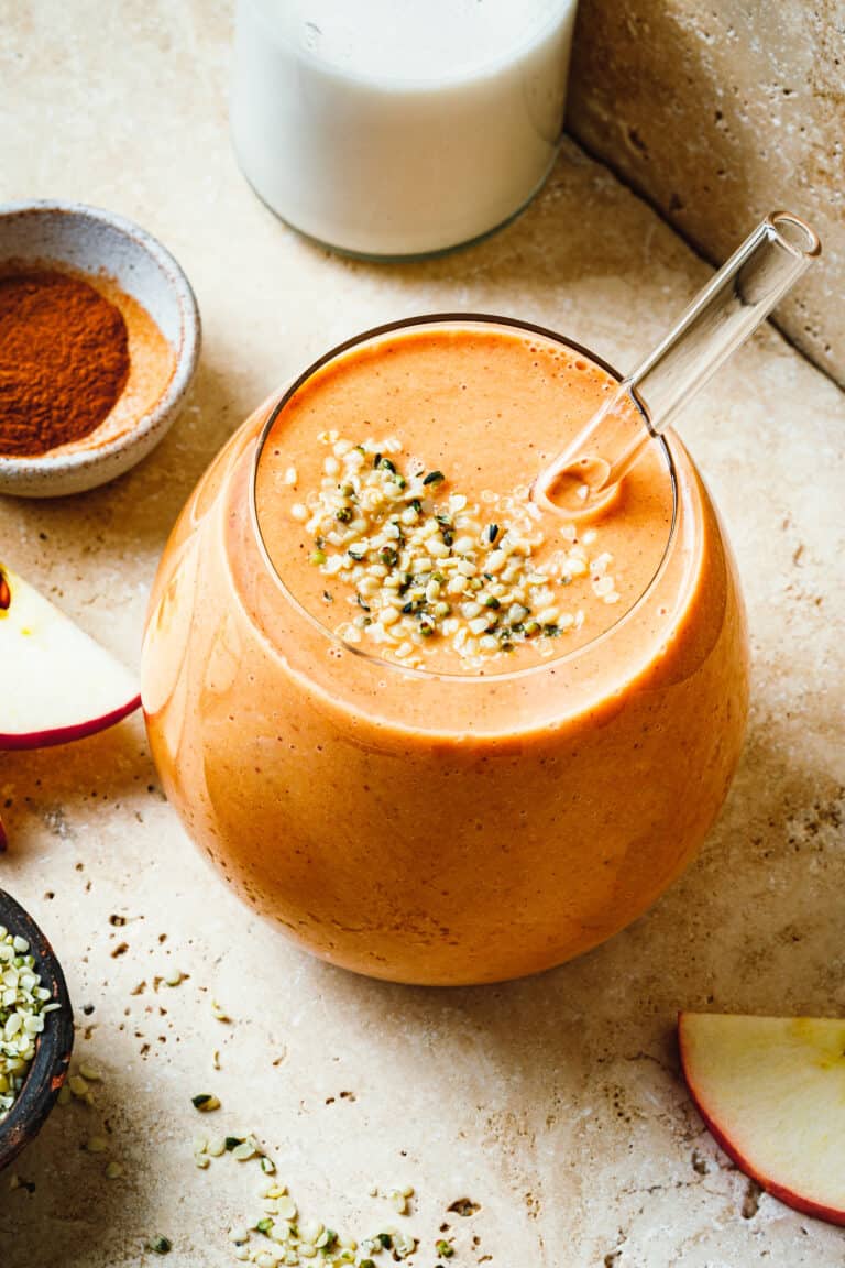 A close-up image of a glass of the sweet potato apple pie smoothie , topped with hemp seeds and a straw