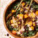 A large bowl of the winter kale salad, sitting on a countertop with golden spoons and forks placed into it