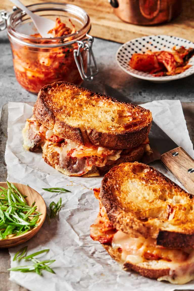 Two of the kimchi grilled cheese sandwiches, laid out on a sheet of parchment paper on a countertop