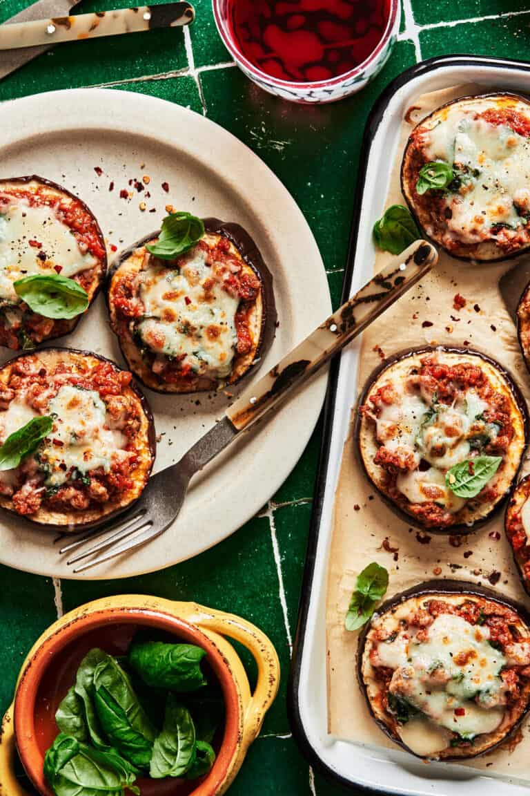 A plate of the mini eggplant pizzas, sitting on a countertop next to a tray of more of the pizzas