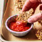 A close-up image of one of the crispy artichoke hearts, being dipped into a small bowl of marinara sauce