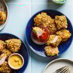 A plate of the oven baked pickle brined chicken nuggets, sitting on a countertop alongside a bowl of ketchup and a drink