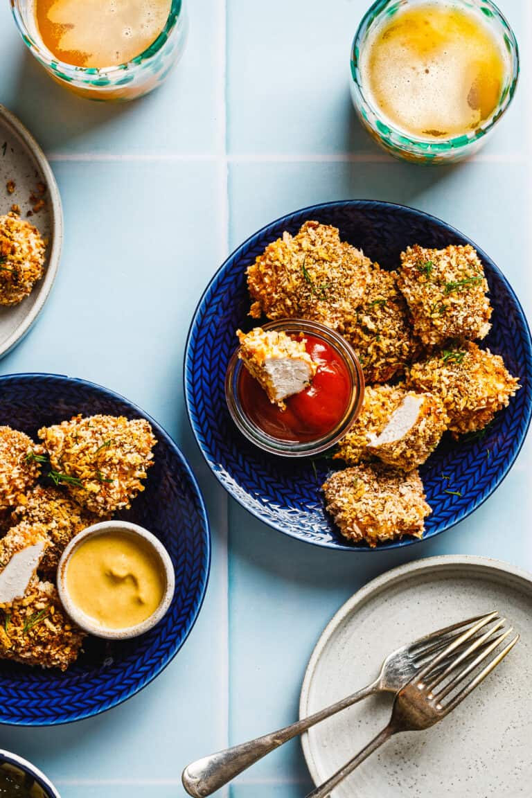 A plate of the oven baked pickle brined chicken nuggets, sitting on a countertop alongside a bowl of ketchup and a drink