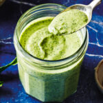 A jar of the ultimate green goddess dressing, with a spoon dipped into it