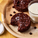 A close-up image of one of the Star Crunch clusters, with a bite taken out of it, sitting on a plate alongside a glass of milk