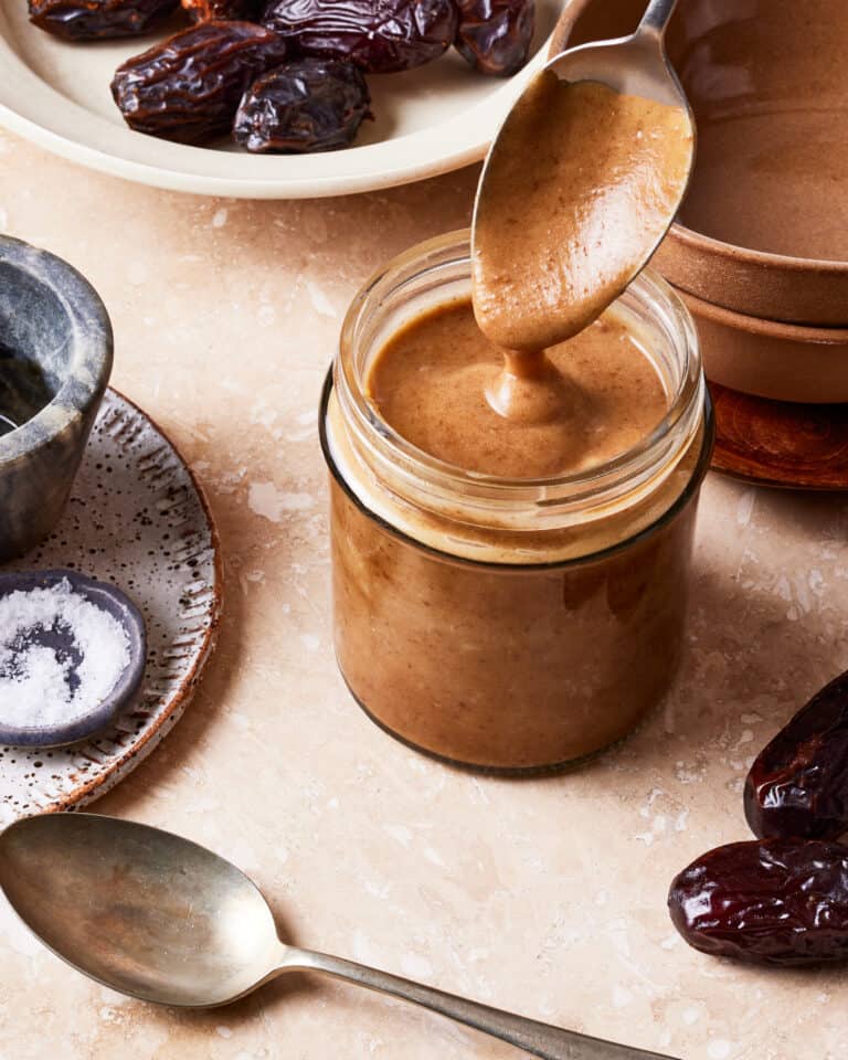 A jar of the date sweetened caramel sauce, with a spoon actively taking out some of the jar