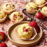 One of the simple strawberry muffins, sitting on a plate with some more of the muffins in the background