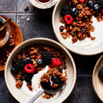 Two bowls of the breakfast quinoa, topped with berries and yogurt and spread out on a countertop