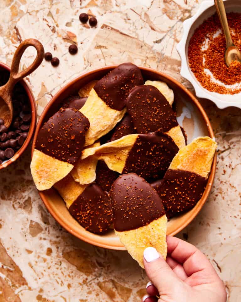 A plate of the chocolate dipped mango with tajin, sitting on a countertop with a hand reaching for one of the slices